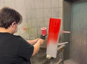 Ein Junge lackter einen Gegenstand mit roter Farbe beim Lackierworkshop.